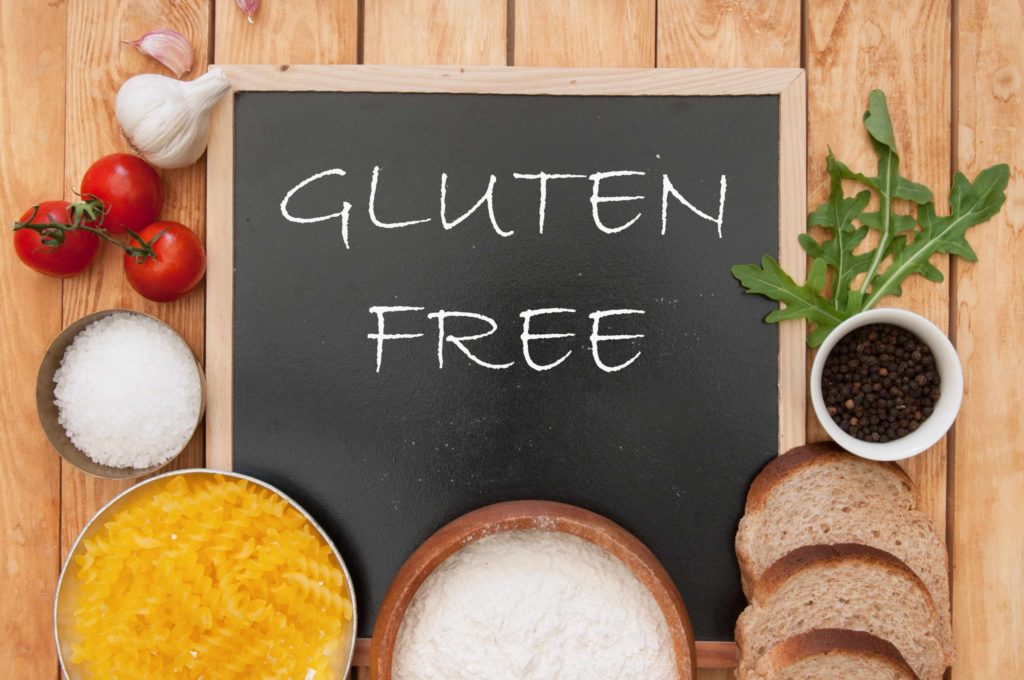 Various foods surrounding a chalkboard that has "Gluten Free" written on it