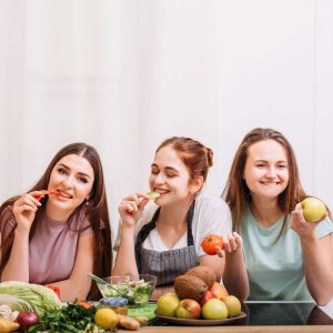 3 girls smiling and eating fruit and vegetables